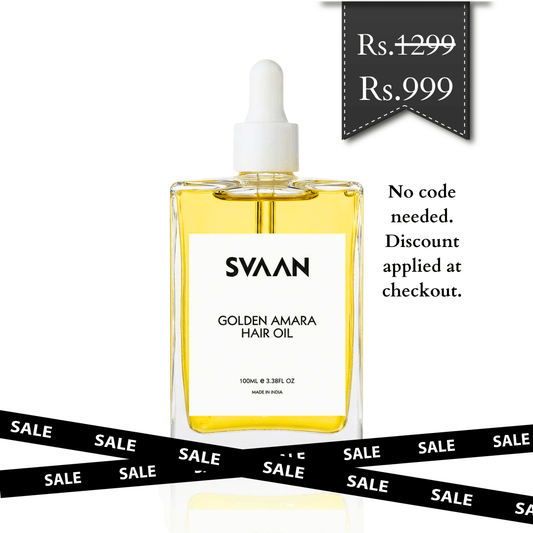 A promotional image featuring a clear square glass bottle of Svaan Golden Amara Hair Oil filled with golden liquid and topped with a white dropper. In the top right corner, a dark grey banner shows a crossed-out original price of Rs. 1299 and a sale price of Rs. 999. Text beside the bottle reads, "No code needed. Discount applied at checkout." Two black ribbons with the word "SALE" in white crisscross across the bottom of the white background.