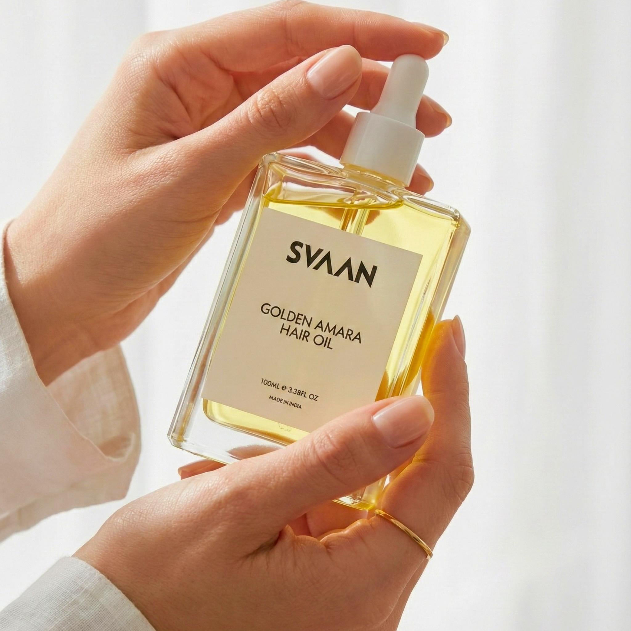 A women's hands holding a bottle of golden amara hair oil.
