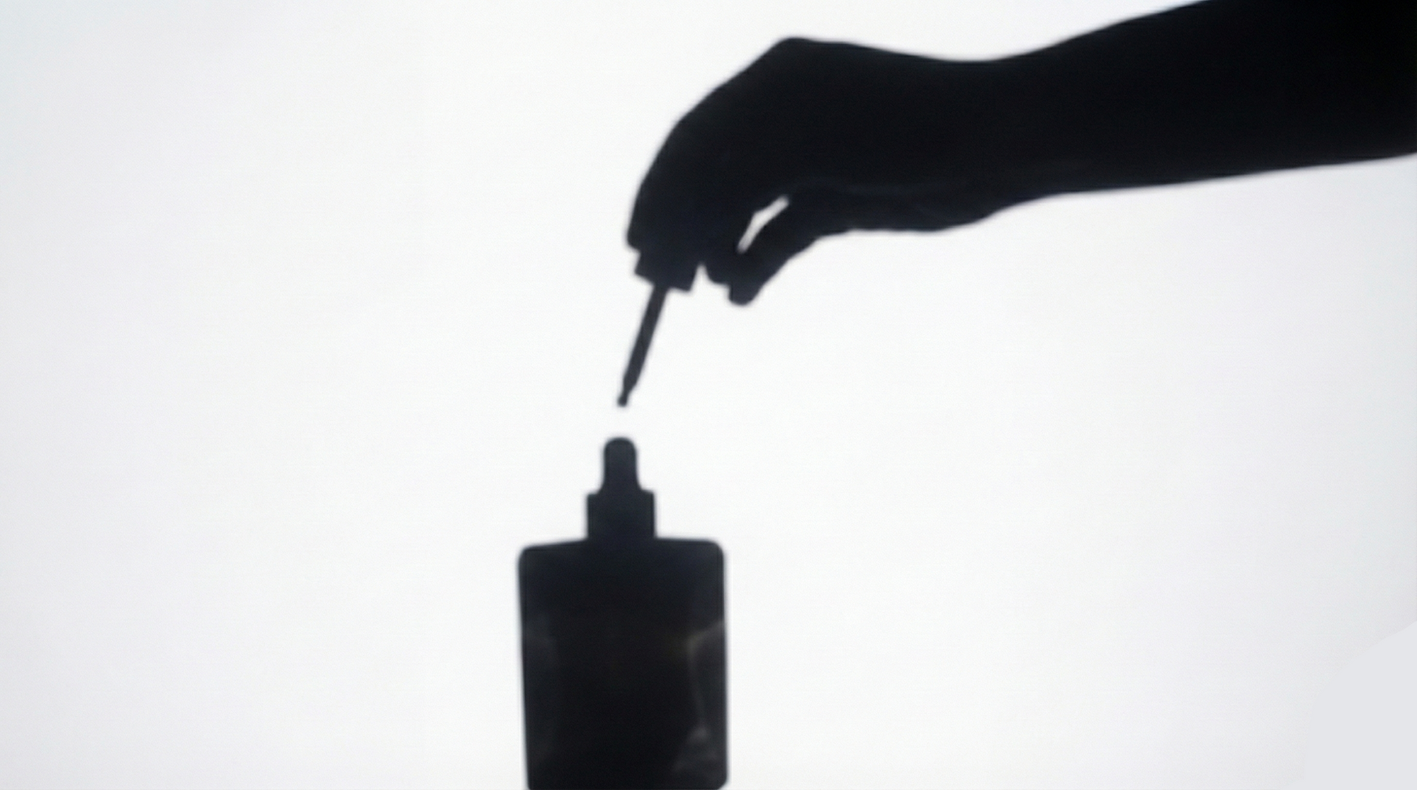 Silhouette of a hand holding a dropper over a bottle of golden amara on a white background
